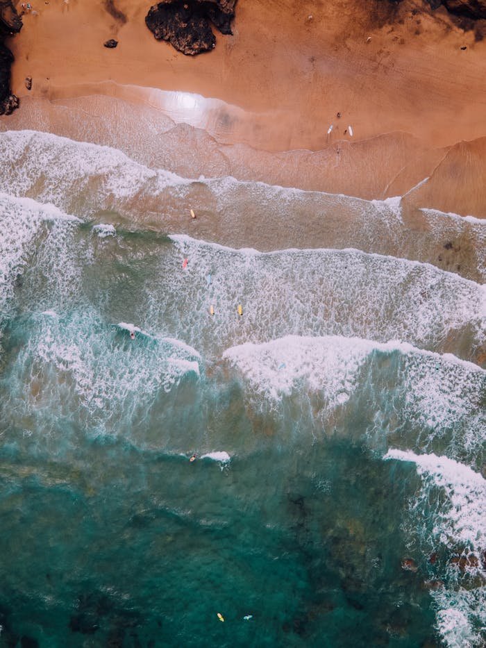 Stunning aerial shot of surfers riding waves on a sandy beach in Spain.